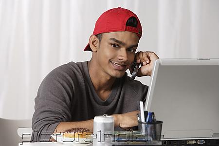 PictureIndia - young man with red cap, talking on phone and working on laptop