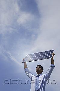 PictureIndia - Businessman holding solar panel outside.