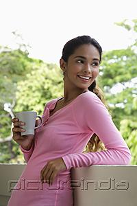 PictureIndia - Young woman holding mug looking over shoulder