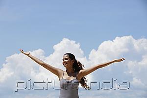PictureIndia - young woman lifting up her arms with blue sky and clouds background
