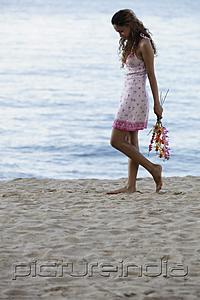 PictureIndia - young woman walking on beach holding pink flowers