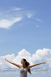 PictureIndia - happy young woman raising her arms, blue sky and clouds background.