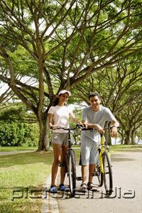PictureIndia - Couple standing with bicycles in park, looking at camera