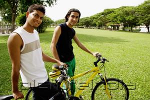 PictureIndia - Two young men on bicycles in park, smiling at camera