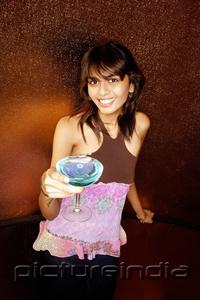 PictureIndia - Young woman holding drink, looking at camera