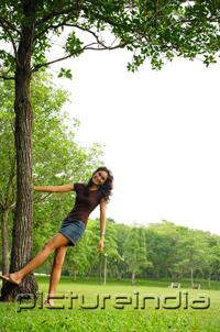 PictureIndia - Young woman standing with hand on tree, smiling at camera