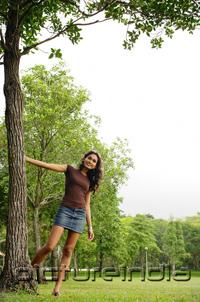 PictureIndia - Young woman standing with hand on tree, smiling at camera
