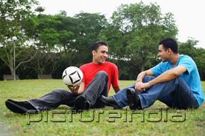 PictureIndia - Two men sitting on grass, talking, one holding soccer ball