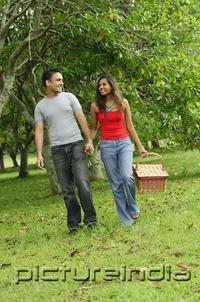 PictureIndia - Couple walking in park, holding hands, woman carrying picnic basket