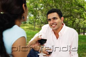 PictureIndia - Couple holding wine glasses in park, over the shoulder view