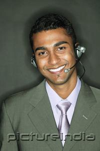 PictureIndia - Businessman using headset, looking at camera