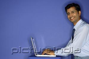 PictureIndia - Man using laptop, smiling at camera