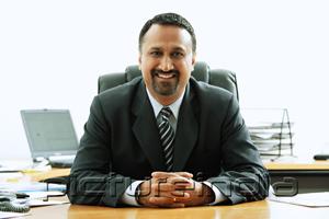 PictureIndia - Businessman at desk, smiling at camera, hands clasped