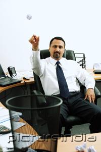 PictureIndia - Businessman sitting in office throwing paper ball into dustbin