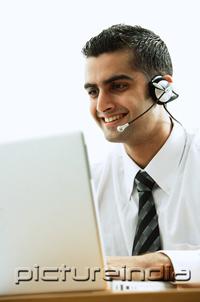 PictureIndia - Executive using headset, smiling, using laptop
