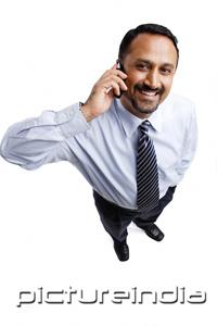 PictureIndia - Businessman using mobile phone, looking at camera