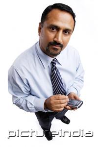 PictureIndia - Businessman using PDA, looking at camera