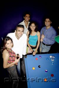 PictureIndia - Young adults standing around pool table, smiling at camera