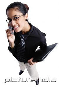 PictureIndia - Business woman using mobile phone, smiling at camera, high angle view