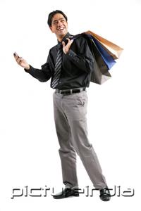 PictureIndia - Businessman carrying shopping bags over shoulder, holding mobile phone