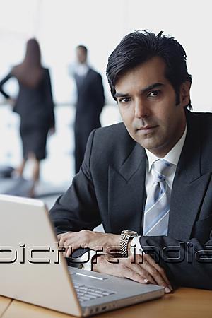 PictureIndia - Businessman sitting in front of laptop, looking at camera