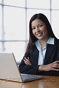 PictureIndia - Businesswoman sitting in front of laptop, arms crossed, smiling