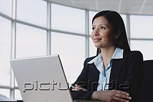 PictureIndia - Businesswoman sitting in front of laptop, arms crossed, looking away