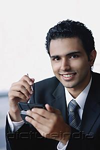 PictureIndia - Young businessman with mobile phone, smiling at camera
